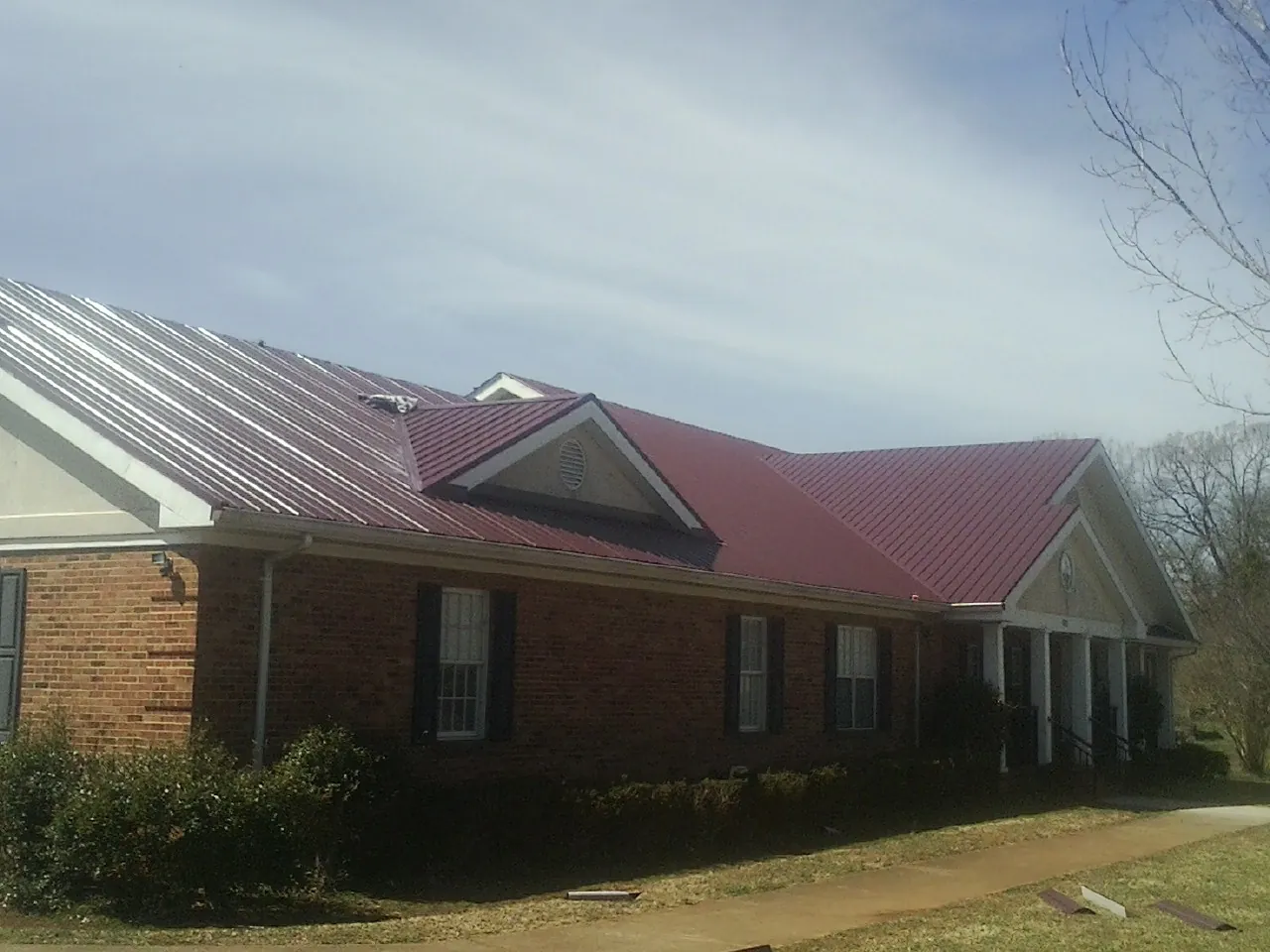 Red metal roof with gabled entries on a long brick building, from a Hail Damage Roof Repair job in Monson