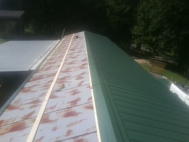 Old rusted panels beside newly installed green metal roofing — Wind Damage Roof Repair by Roofing Brothers in Monson