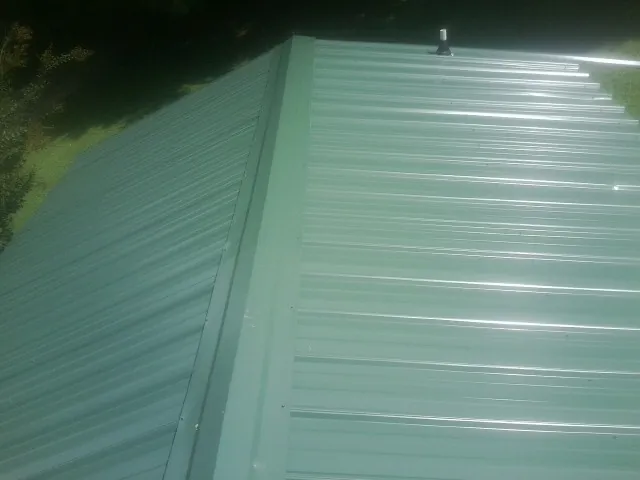 New green metal panels meeting at the ridge of a roof — Flat Roof Repair work by our crew in Monson