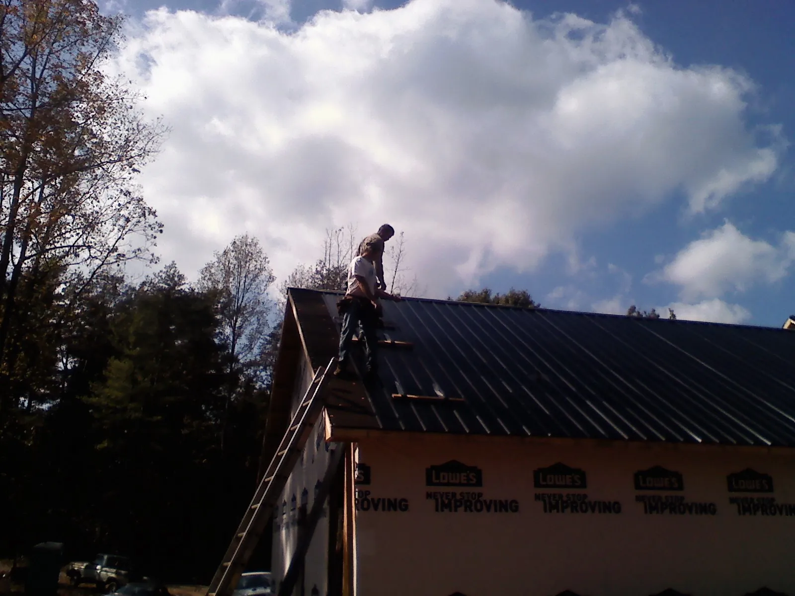 Roofer fastening dark metal panels high against a cloudy sky, from a Roof Inspection job in Monson