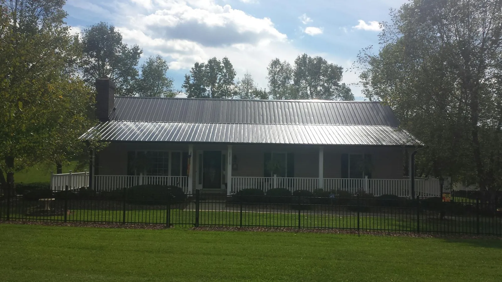 Gray metal roof on a brick ranch with a full width front porch — Gutter Guard Installation work by our crew in Monson