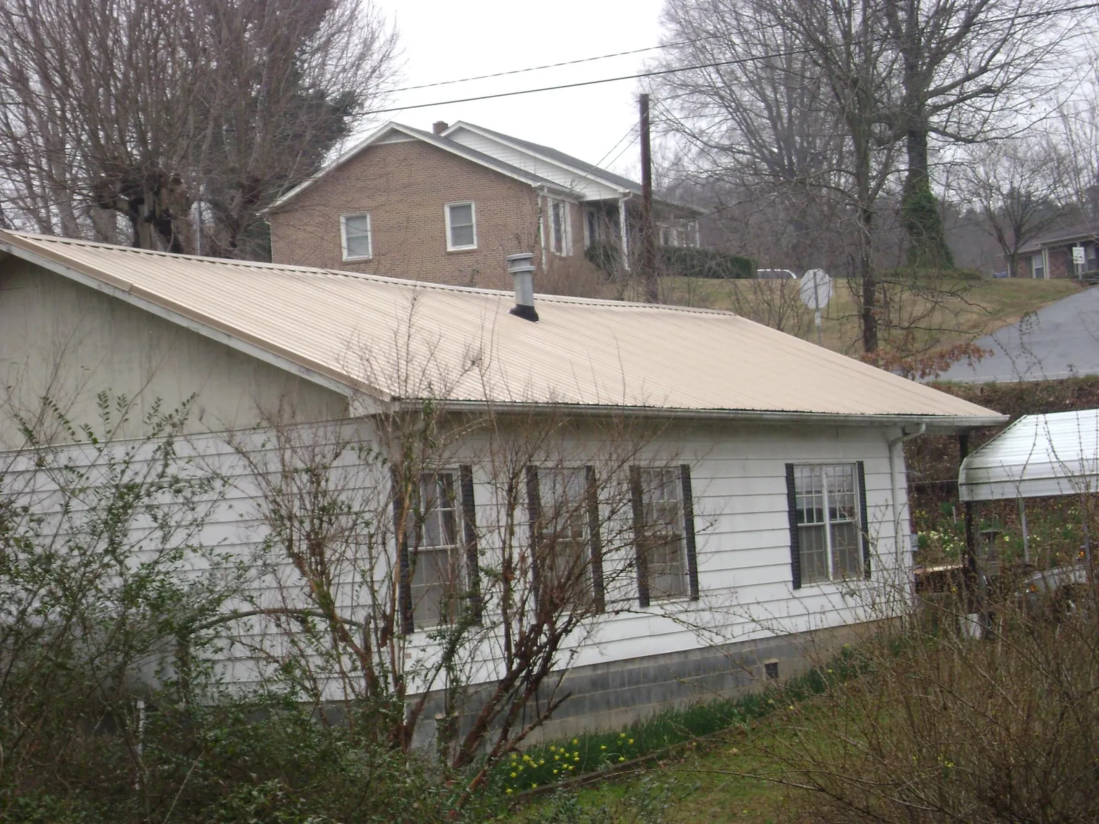 Tan metal roof on a white sided house set into a hillside — Commercial Roofing by Roofing Brothers in Monson