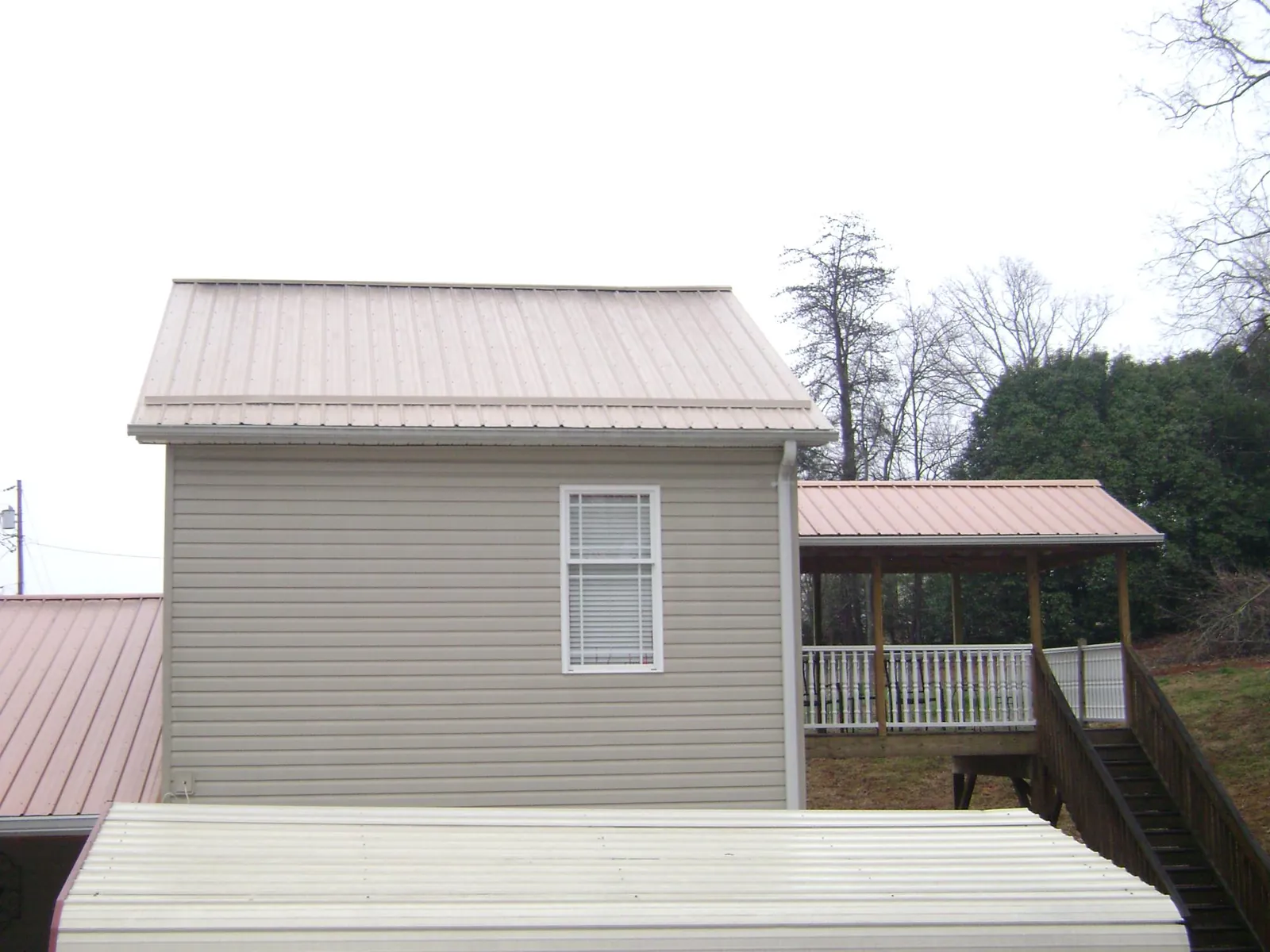 Tan metal roofs on a two story addition and attached porch, from a Roof Replacement job in Monson